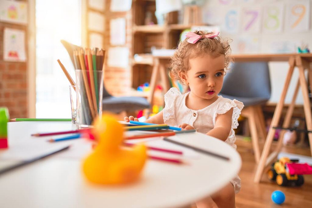 Bela criança caucasiana brincando com brinquedos na sala de jogos colorida. Desenho feliz e brincalhão com lápis de cor no jardim de infância
. - Foto, Imagem