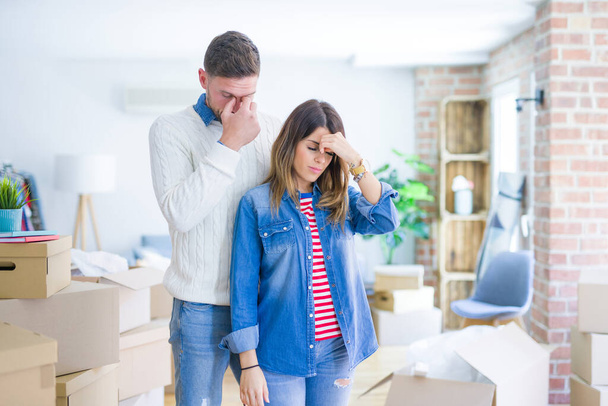 Young beautiful couple standing at new home around cardboard boxes tired rubbing nose and eyes feeling fatigue and headache. Stress and frustration concept. - Photo, Image