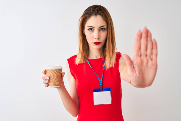 Rudowłosa bizneswoman noszenie id karty picia filiżanki kawy na izolowanym białym tle z otwartą ręką robi znak stop z poważnym i pewnym siebie wyrazem twarzy, gest obrony - Zdjęcie, obraz