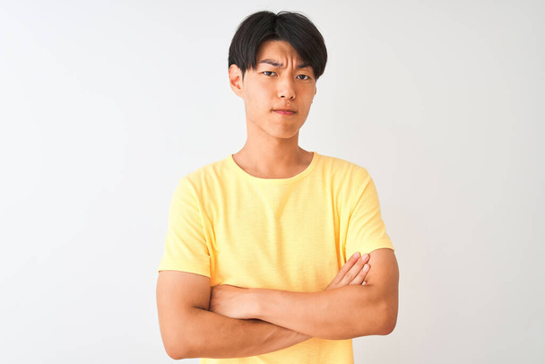 Chinese man wearing yellow casual t-shirt standing over isolated white background skeptic and nervous, disapproving expression on face with crossed arms. Negative person. - Photo, Image