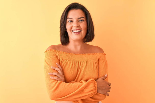 Jonge mooie vrouw met casual t-shirt over geïsoleerde oranje achtergrond vrolijk gezicht glimlachend met gekruiste armen kijkend naar de camera. Positief persoon. - Foto, afbeelding