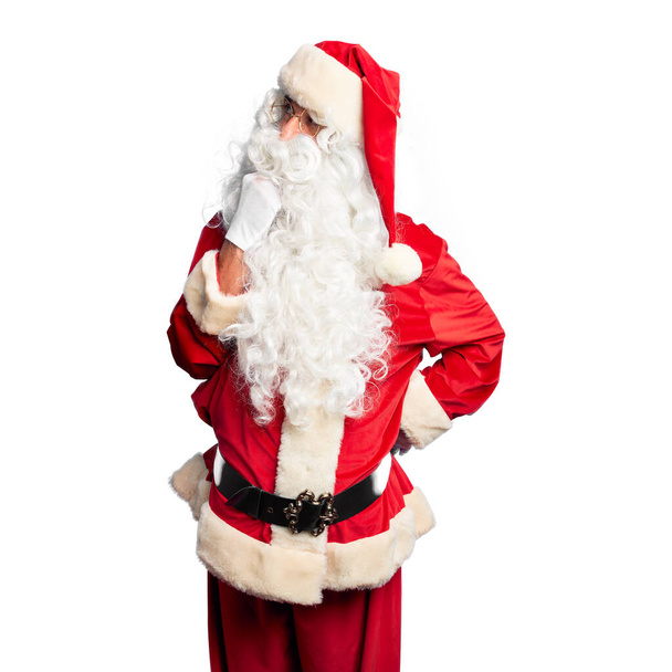 Ein gutaussehender Mann mittleren Alters im Weihnachtsmann-Kostüm und Bart, der mit der Hand am Kinn über Fragen nachdenkt, nachdenklichen Ausdruck. Lächeln mit nachdenklichem Gesicht. Zweifelhaftes Konzept. - Foto, Bild