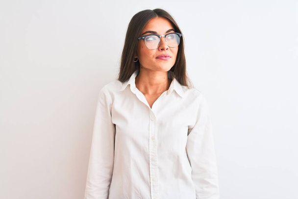 Νεαρή όμορφη επιχειρηματίας φορώντας γυαλιά στέκεται πάνω από απομονωμένο λευκό φόντο χαμογελώντας κοιτάζοντας στο πλάι και κοιτάζοντας μακριά σκέψης. - Φωτογραφία, εικόνα