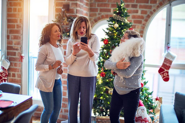 Femmes d'âge moyen souriant heureux et confiant. Tenant debout chien faire selfie par smartphone autour de l'arbre de Noël
 - Photo, image