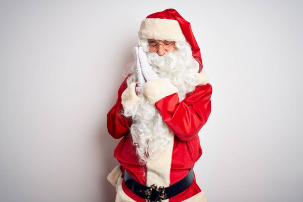 gutaussehender Mann mittleren Alters im Weihnachtsmannkostüm, der vor isoliertem weißen Hintergrund steht und müde träumt und mit geschlossenen Augen lächelnd mit den Händen posiert. - Foto, Bild