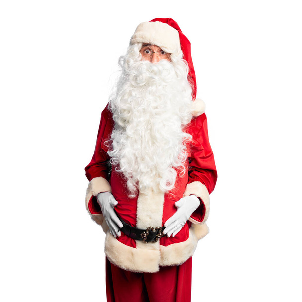 Middelbare leeftijd knappe man in Santa Claus kostuum en baard staande puffende wangen met grappig gezicht. Mond opgeblazen met lucht, gekke uitdrukking. - Foto, afbeelding