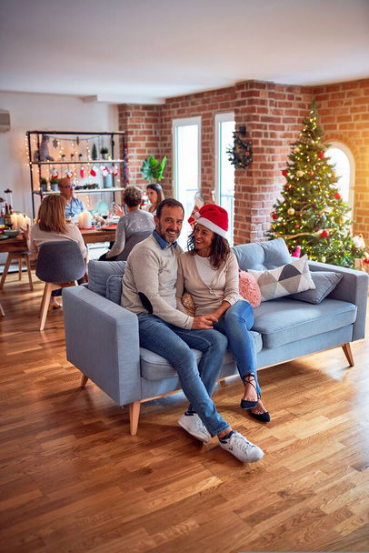 Familie en vrienden dineren thuis om kerst te vieren met traditioneel eten en decoratie, romantisch stel dat samen op de bank zit te praten - Foto, afbeelding