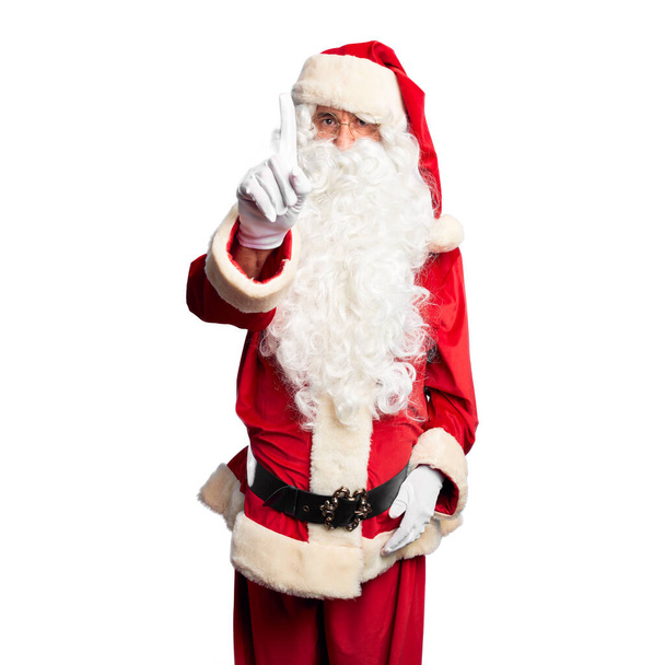 Przystojny mężczyzna w średnim wieku ubrany w kostium Świętego Mikołaja i brodę na stojąco, wskazujący palcem w górę i gniewnym wyrazem twarzy, nie pokazujący gestu - Zdjęcie, obraz