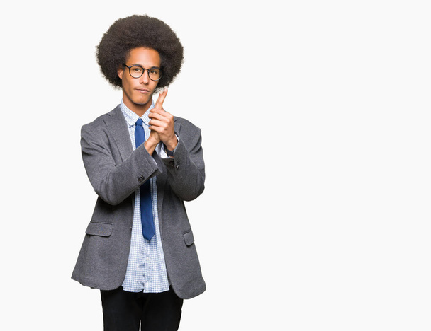 Joven hombre de negocios afroamericano con cabello afro usando gafas sosteniendo arma simbólica con gesto de mano, jugando a matar armas de fuego, cara enojada
 - Foto, Imagen