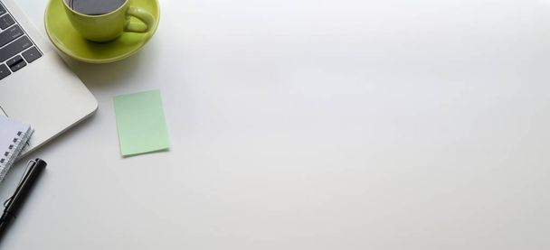 Horní pohled na moderní pracoviště s notebookem a zeleným šálkem kávy na bílém stole a lepkavou poznámkou - Fotografie, Obrázek