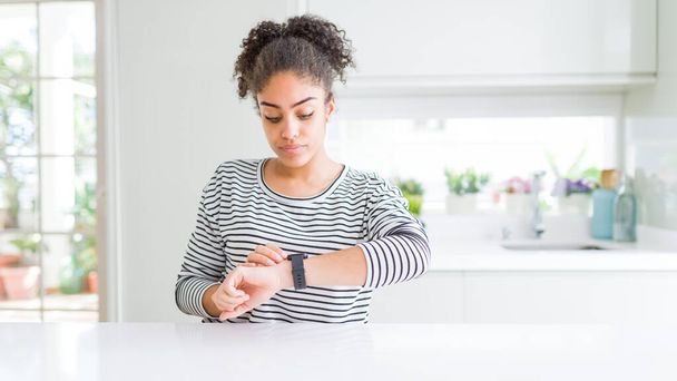 Beautiful african american woman with afro hair wearing casual striped sweater Checking the time on wrist watch, relaxed and confident - Foto, afbeelding