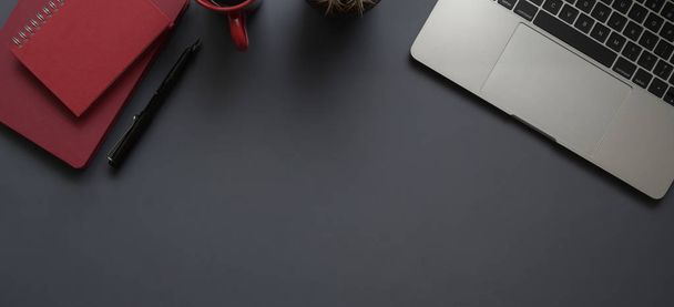 Вид сверху на темное современное рабочее место с ноутбуком, канцелярскими принадлежностями и красной тетрадью с копировальным пространством на сером фоне
 - Фото, изображение