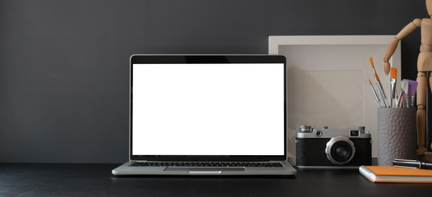 黒の机の上にラップトップコンピュータとカメラとオフィス用品と暗い灰色の壁と暗い現代のワークスペース  - 写真・画像