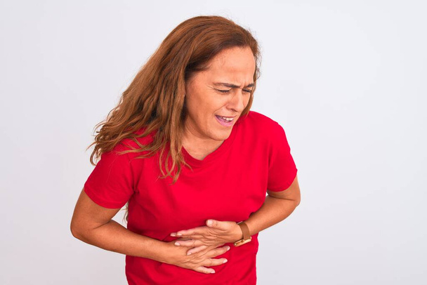 Middle age mature woman standing over white isolated background with hand on stomach because indigestion, painful illness feeling unwell. Ache concept. - Photo, Image