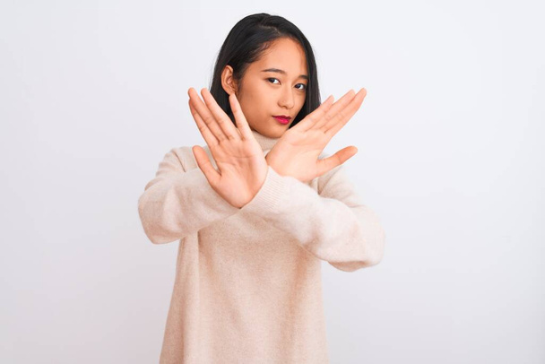 Νεαρή Κινέζα γυναίκα φορώντας ζιβάγκο πουλόβερ στέκεται πάνω από απομονωμένο λευκό φόντο Έκφραση απόρριψης διασχίζει τα χέρια και τις παλάμες κάνει αρνητικό σημάδι, θυμωμένος πρόσωπο - Φωτογραφία, εικόνα