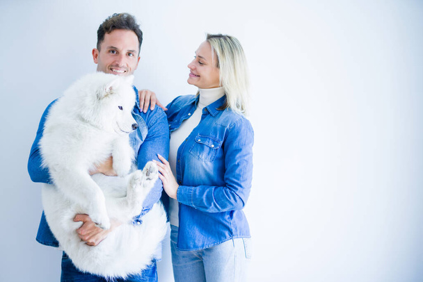 Young beautiful couple holding dog standing over isolated white background - Fotoğraf, Görsel