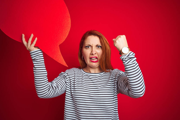 Young beautiful redhead woman holding speech bubble over red isolated background annoyed and frustrated shouting with anger, crazy and yelling with raised hand, anger concept - Photo, Image