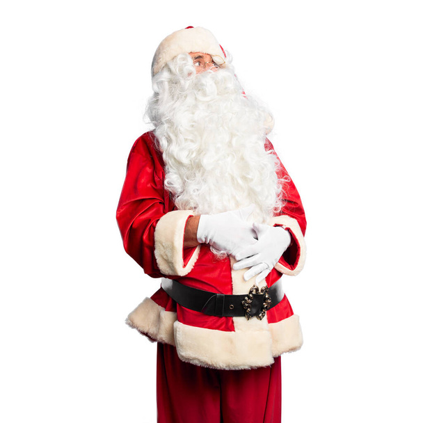 gutaussehender Mann mittleren Alters im Weihnachtsmann-Kostüm und Bart, der mit verschränkten Armen zur Seite schaut und überzeugt und selbstbewusst ist - Foto, Bild
