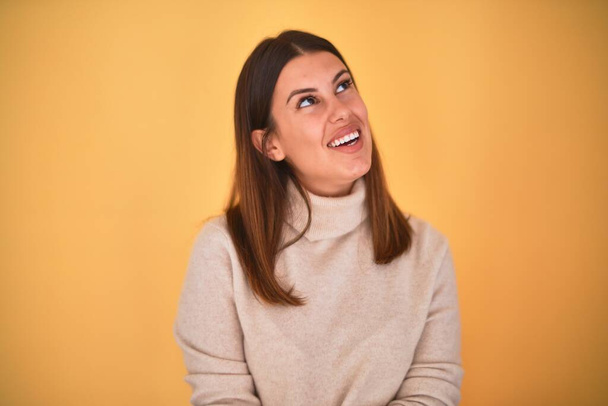 Молода красива жінка, посміхаючись щаслива в светрі над ізольованим жовтим тлом
 - Фото, зображення
