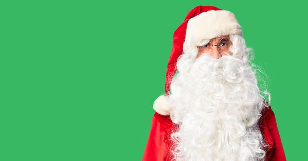 Ein gutaussehender Mann mittleren Alters in Weihnachtsmann-Kostüm und Bart steht entspannt mit ernstem Gesichtsausdruck da. einfacher und natürlicher Blick auf die Kamera. - Foto, Bild