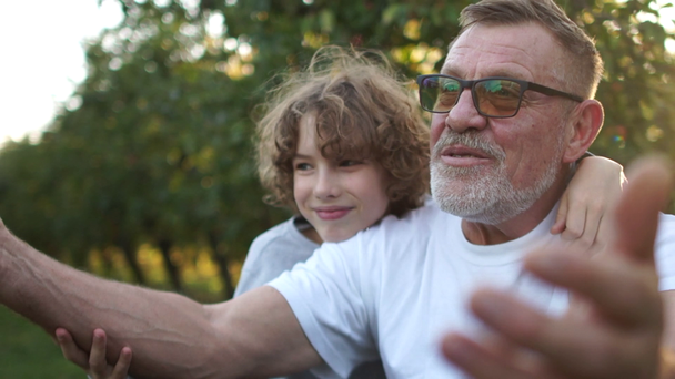 Dziadek i jego wnuki śmieją się radośnie w ogrodzie o zachodzie słońca. wakacje w wiosce, szczęśliwa rodzina, dziecko jedzące jabłko - Materiał filmowy, wideo