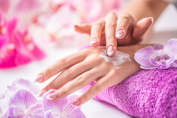 Beautiful female hands applying hand cream. Purple towel and orchid decoration. Healthy concept - Nails spa skin care and wellness - Photo, image