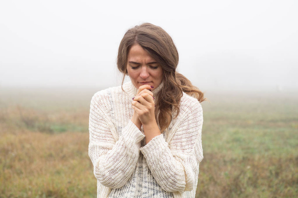 Κορίτσι έκλεισε τα μάτια της, προσεύχεται σε ένα πεδίο κατά τη διάρκεια της όμορφης ομίχλης. Χέρια διπλωμένα στην ιδέα της προσευχής για πίστη - Φωτογραφία, εικόνα