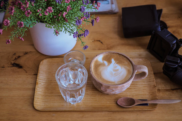 Чашка капучино с искусством латте на деревянной тарелке, стакан воды
 - Фото, изображение