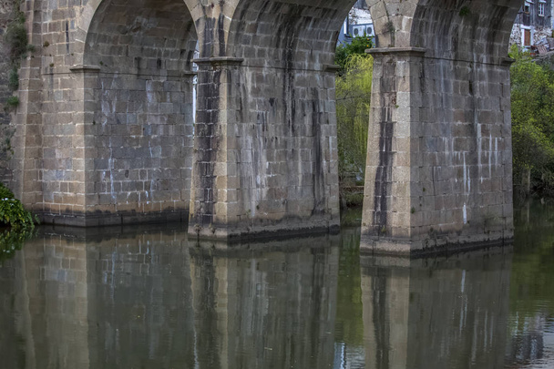 Blick auf die Säulen der alten römischen Brücke über den Fluss, in Stein, mit Vegetation ringsum - Foto, Bild
