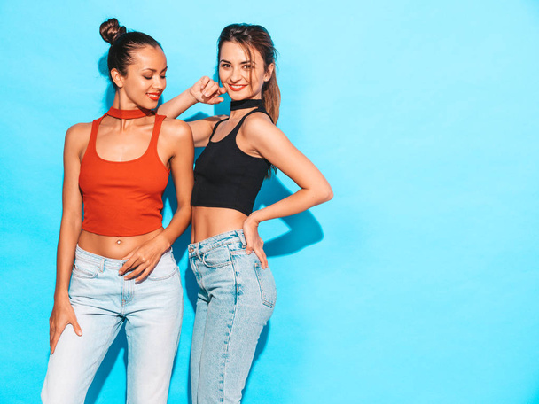 Two young beautiful smiling brunette hipster girls in trendy similar summer colorful shirt clothes.Sexy carefree women posing near blue wall in studio.Positive models having fun - Fotó, kép