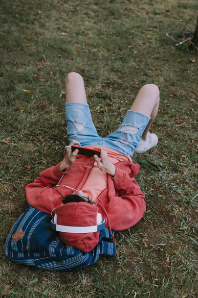 Nuori mies makaa kentällä matkapuhelimen ja kuulokkeiden kanssa
 - Valokuva, kuva