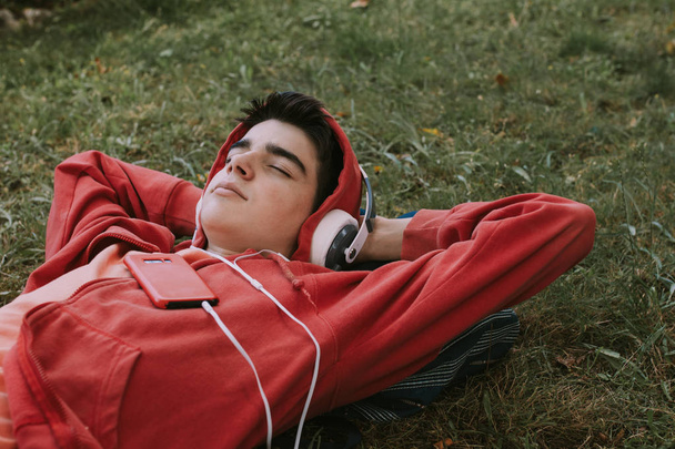 jovem adolescente do sexo masculino com fones de ouvido e telefone deitado no campo
 - Foto, Imagem