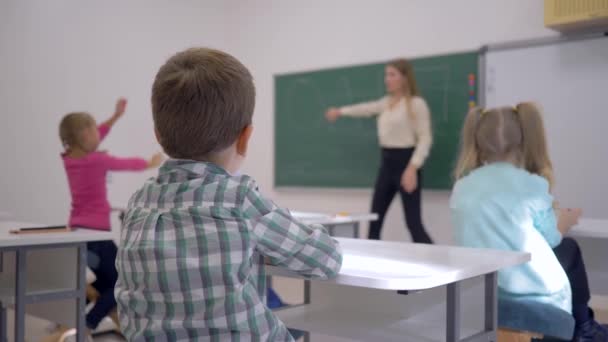 kinderen onderwijs, schoolkinderen bij de les luisteren naar leraar op schoolbord in gericht in de klas van de school - Video