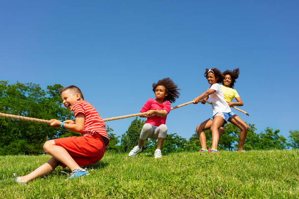 Group of kids pull rope and fall playing competitive game show happy emotion over blue sky in park - Photo, image