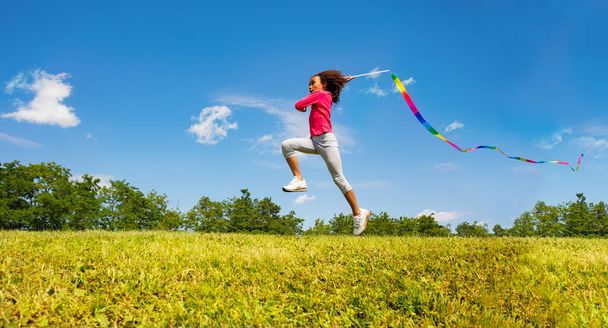 Cute little girl long jump waving with colorful ribbon over field and sky background - 写真・画像