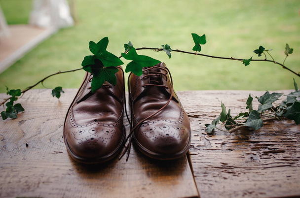 Beautiful brown stylish groom shoes on a wooden table with ivy branch - Photo, Image