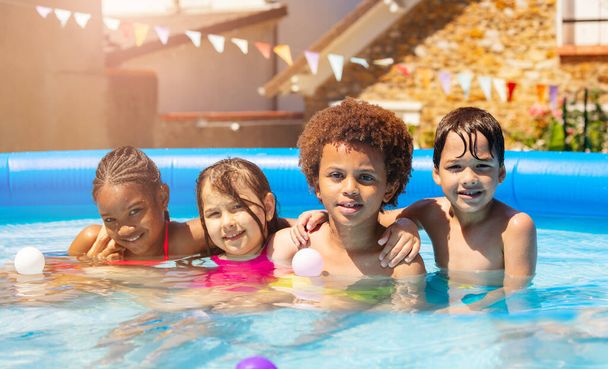 Group of many happy children boys with girls play sit and hug in swimming pool on hot summer day lifting hands up smiling - Foto, Bild