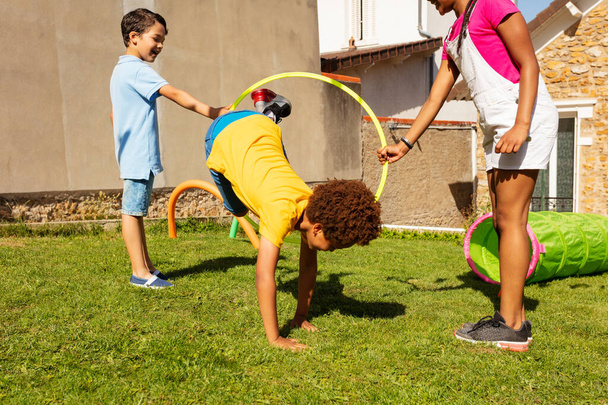 Group of friends play with color sport hoops, handsome black boy jumps inside hold by two kids - Photo, image