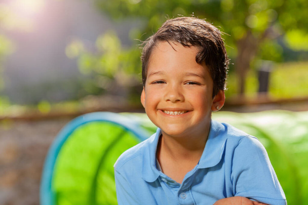 Nice close-up portrait of happy smiling boy in blue shirt on playground on summer day - Fotoğraf, Görsel