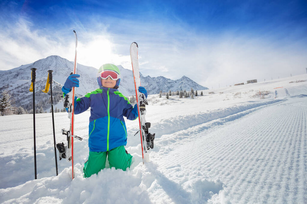 Boy in blue winter clothes with skiing mask and helmet sit on the side of sky slope path piste over high mountain range peaks - Foto, Bild