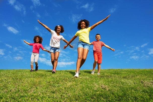 Grupa dzieci z dłońmi w latającej pozie biegać po polu trawy nad niebem - Zdjęcie, obraz