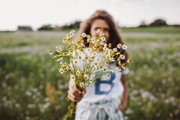 Selective focus shot of a curly model standing in a filed holding a bouquet of daisies - Fotografie, Obrázek