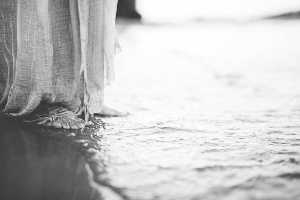 Closeup shot of a person wearing a biblical robe while standing on the shore in black and white - 写真・画像