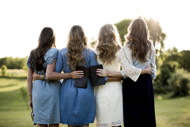Beautiful shot of female with their arms around each other while holding the bible - 写真・画像