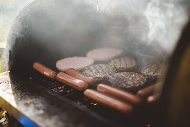 Detailní záběr hovězích hamburgerů na grilu poblíž hot dogů - Fotografie, Obrázek