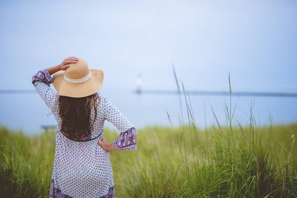 Kobieta w letniej czapce z ręką na biodrze, stojąca z tyłu na trawiastym polu strzału - Zdjęcie, obraz