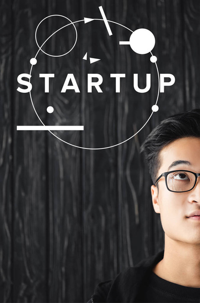 cropped view of asian man in glasses looking at illustration with startup lettering  - Foto, afbeelding