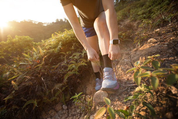 女性トレイルランナー森林歩道上の靴ひもを結ぶ - 写真・画像