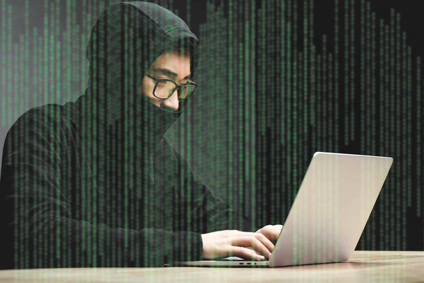 asian hacker in glasses sitting at table, using laptop and surrounded with illustration  - Fotografie, Obrázek