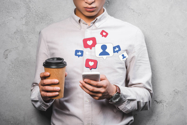 cropped view of seo manager holding paper cup, using smartphone with emojis illustration - Photo, Image